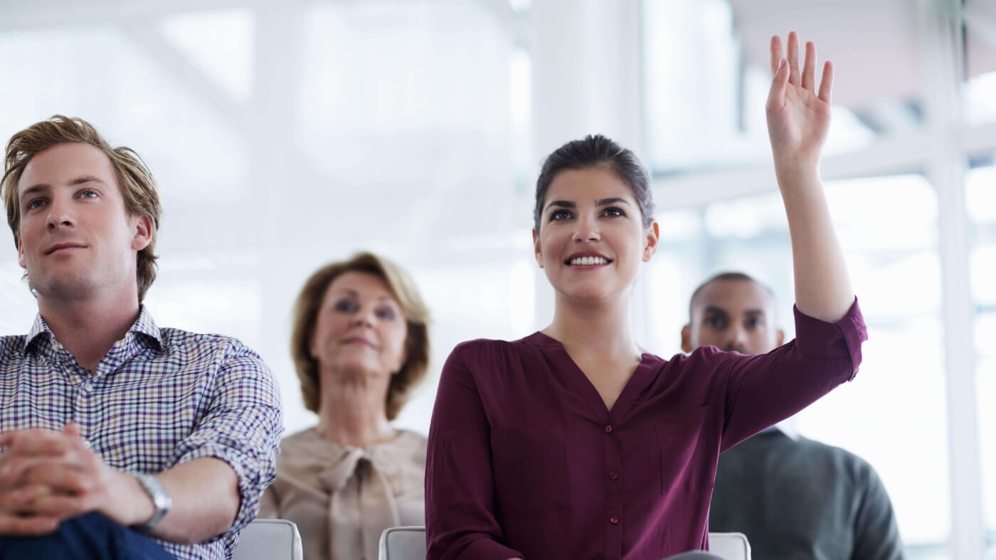 smiling woman raising hand to ask a question in an audience