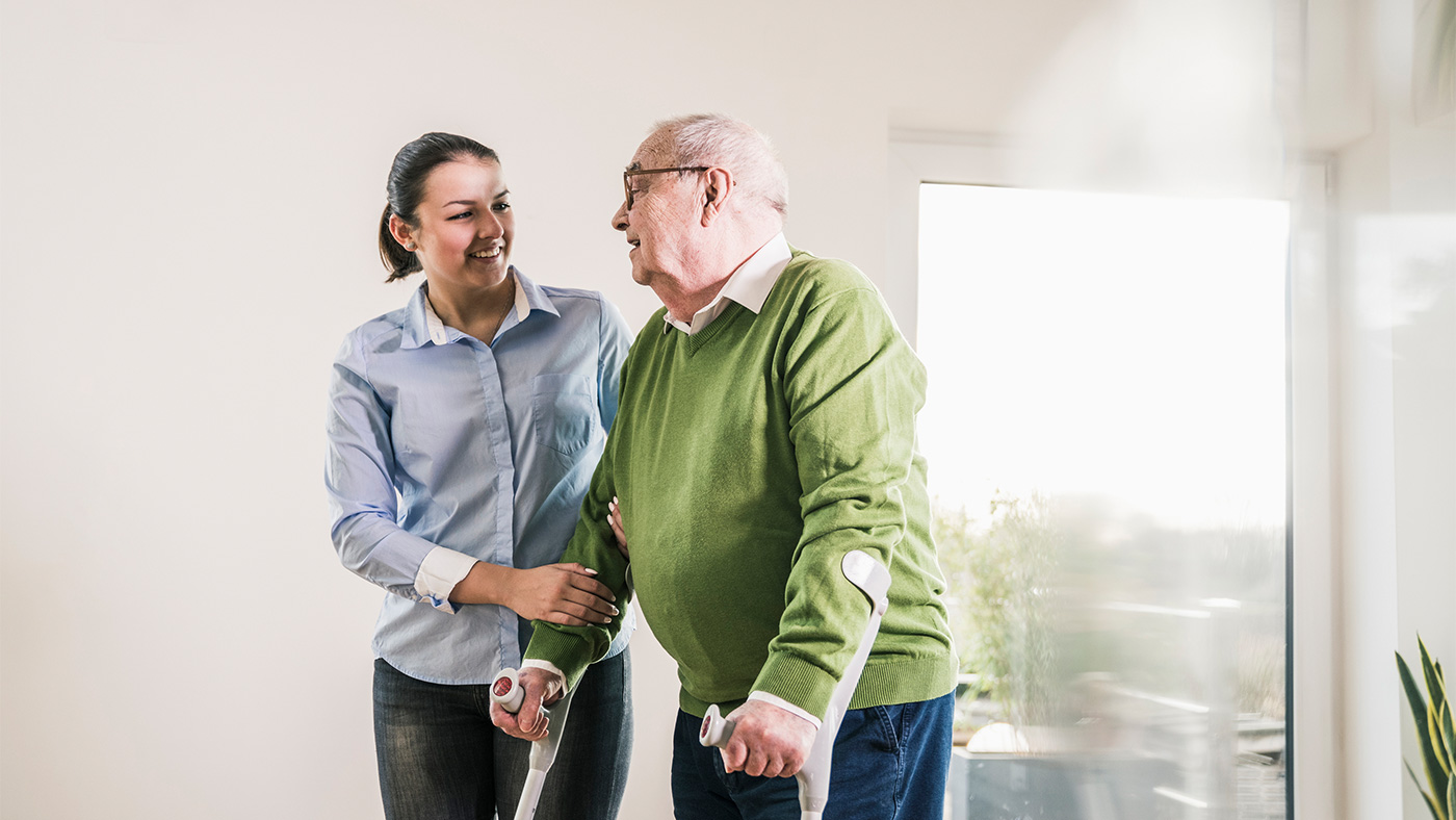 Young woman helping an elderly man on crutches.